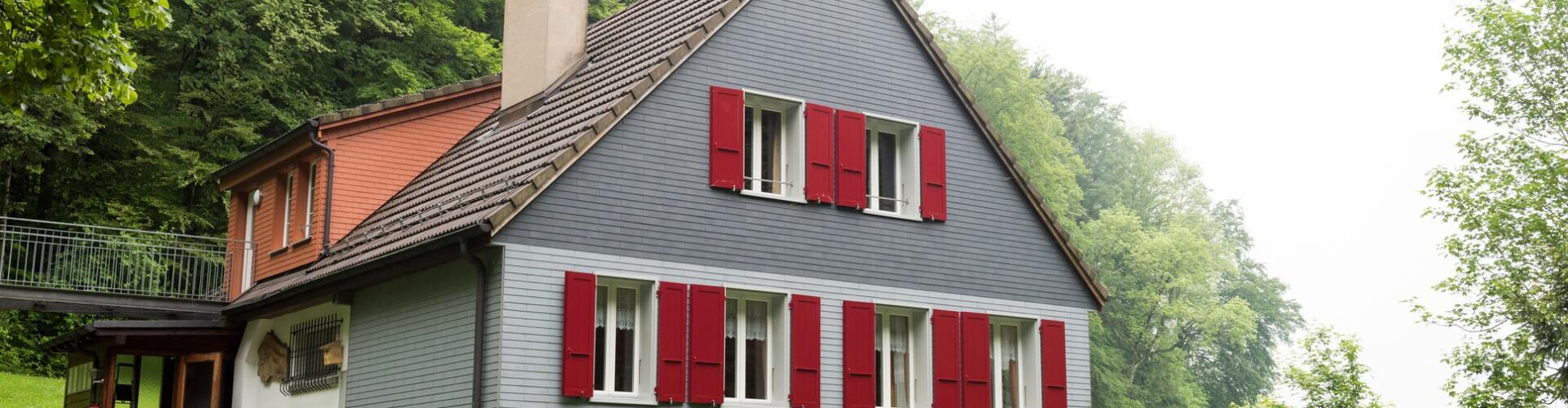 ein Haus mit roten Fensterläden auf einem Hügel